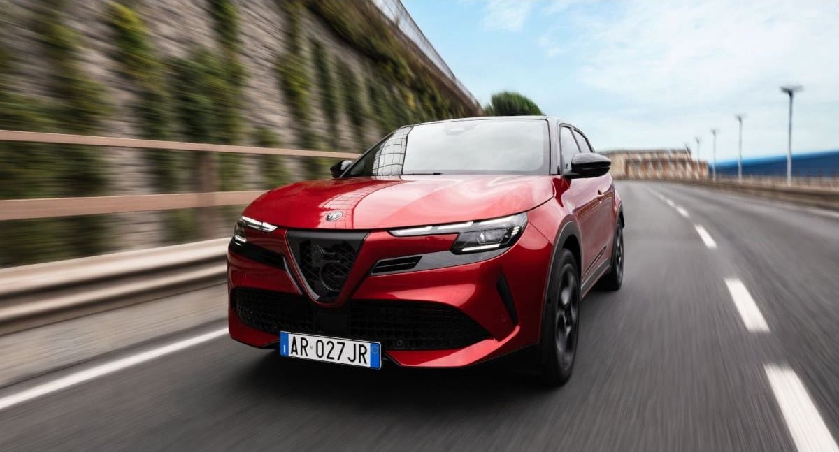 Un Alfa Romeo Junior rojo circula por una carretera junto a un muro de piedra