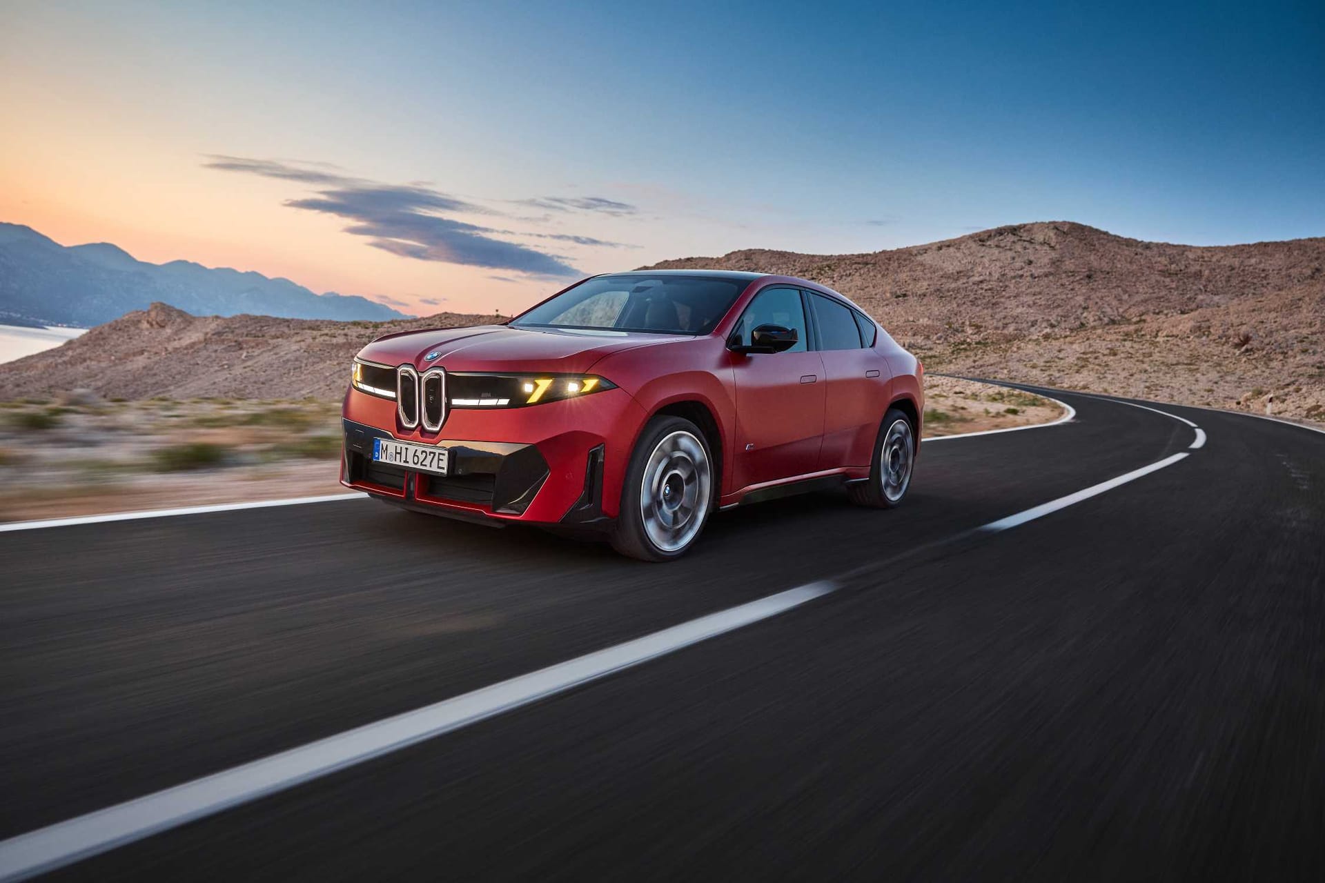 El BMW iX4 M60 xDrive rojo en marcha por una carretera de montaña