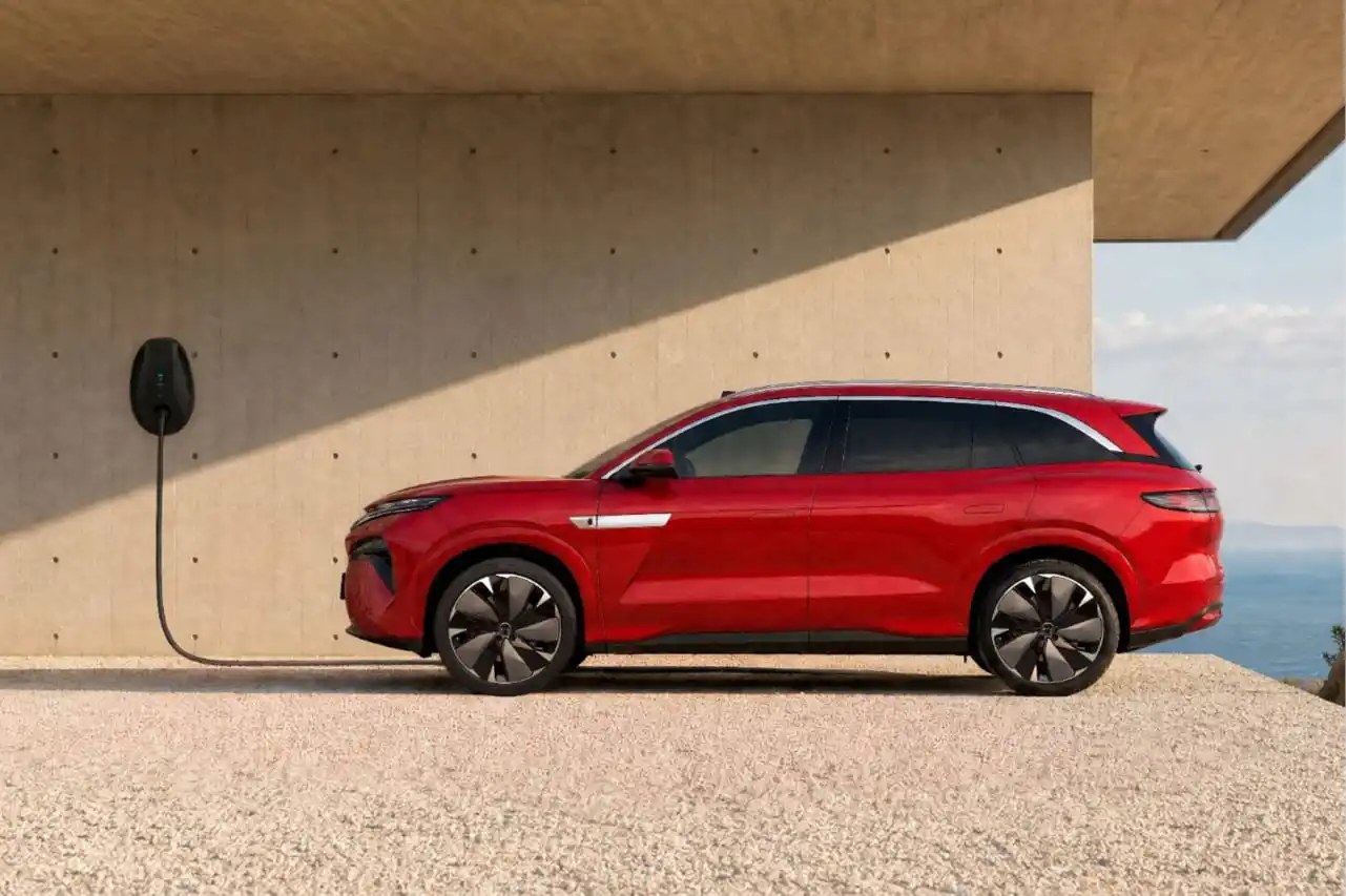 El BYD ATTO 8 de color rojo, de perfil, junto a un punto de carga