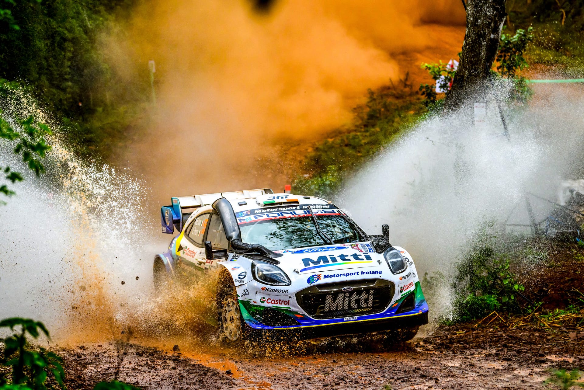 Un Ford Puma Rally1 de M-Sport levanta agua y barro al cruzar un vadeo en un tramo de tierra