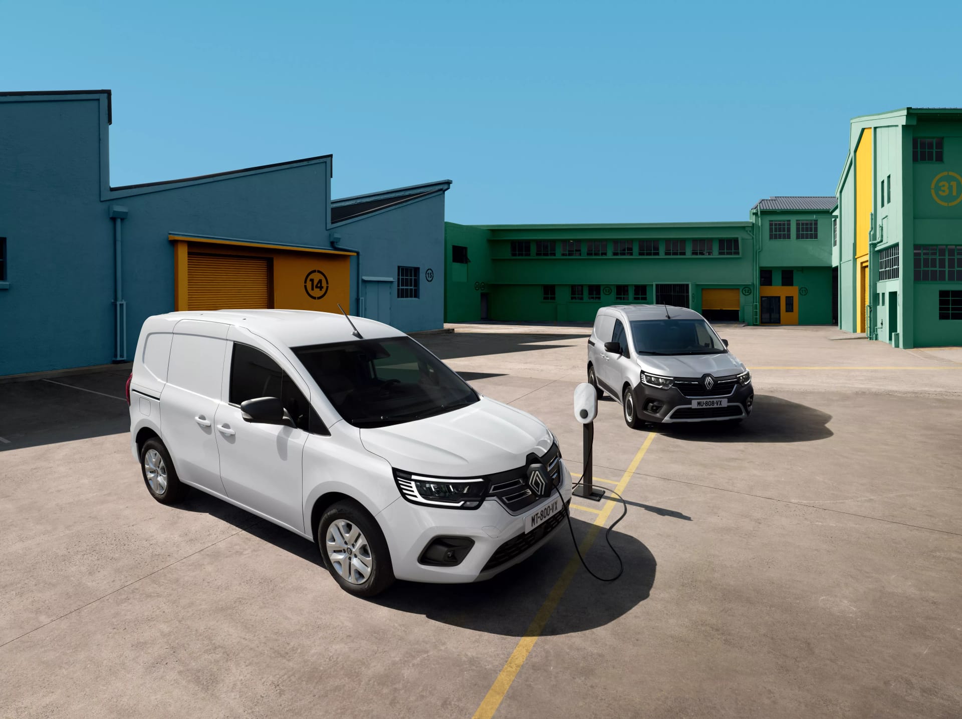 Una Renault Kangoo Furgón blanca y otra cargando en un poste, en un patio industrial
