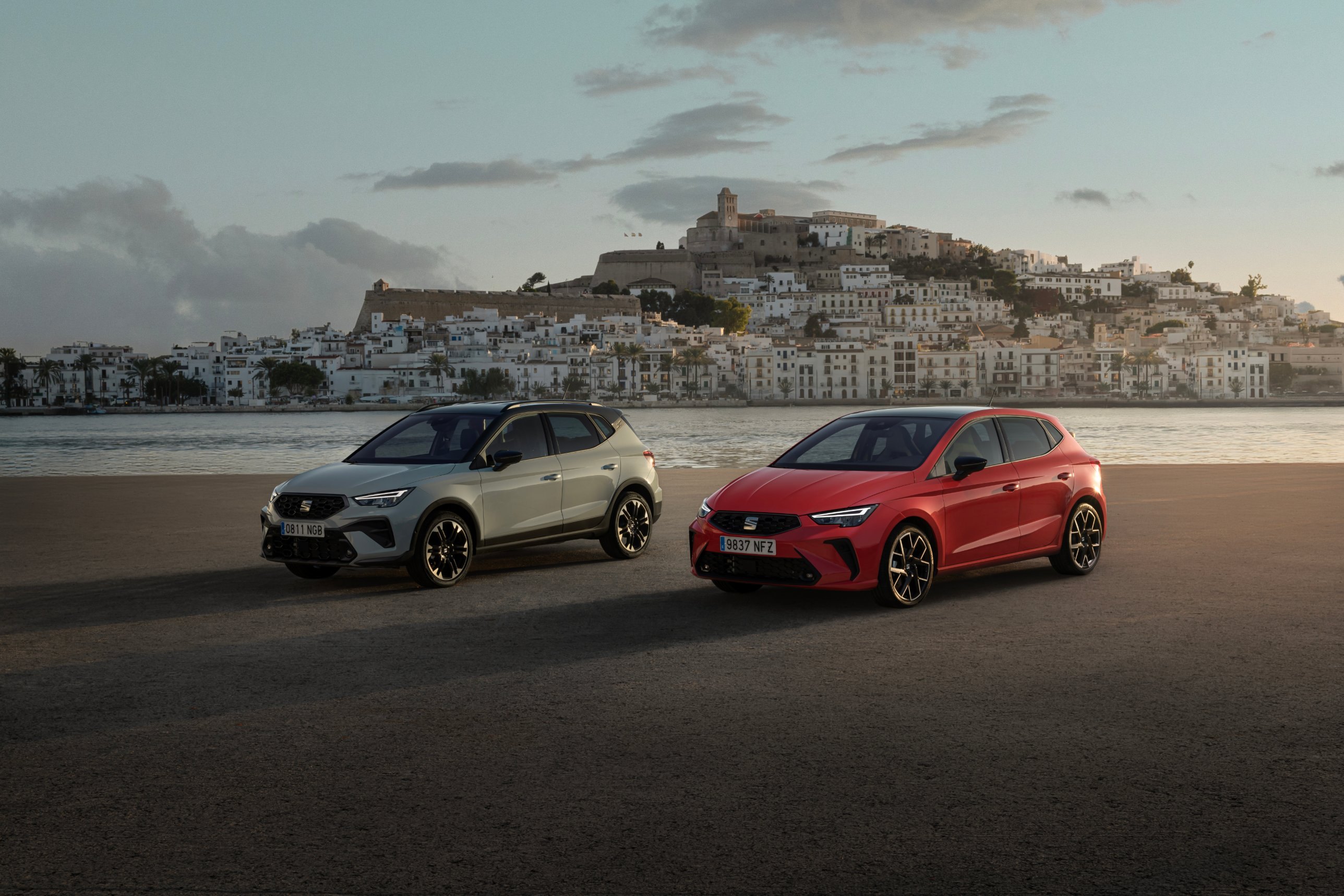 Un SEAT Arona gris y un SEAT Ibiza rojo frente al casco antiguo de Ibiza