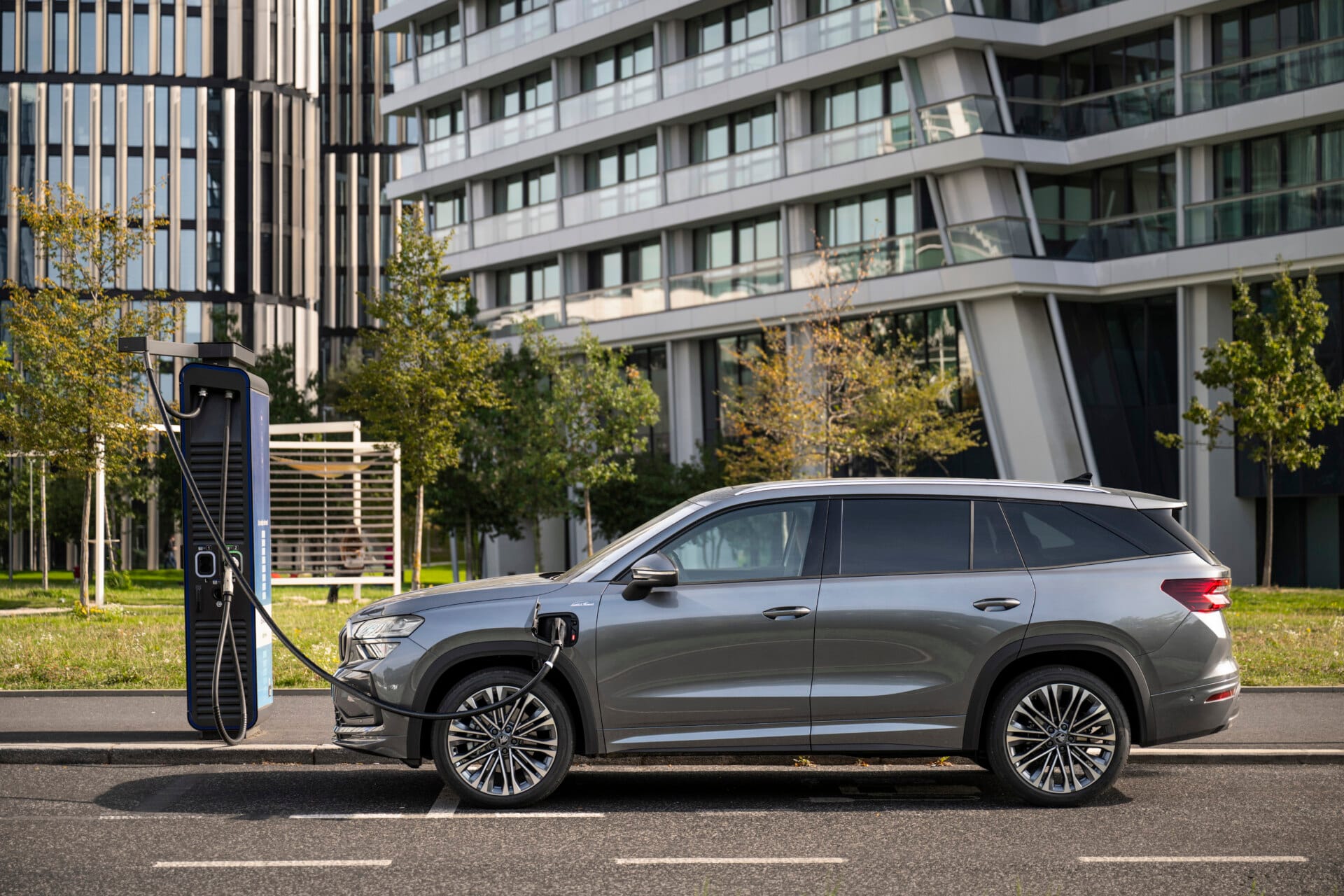 Un Škoda Kodiaq gris cargando en un punto de recarga junto a un edificio
