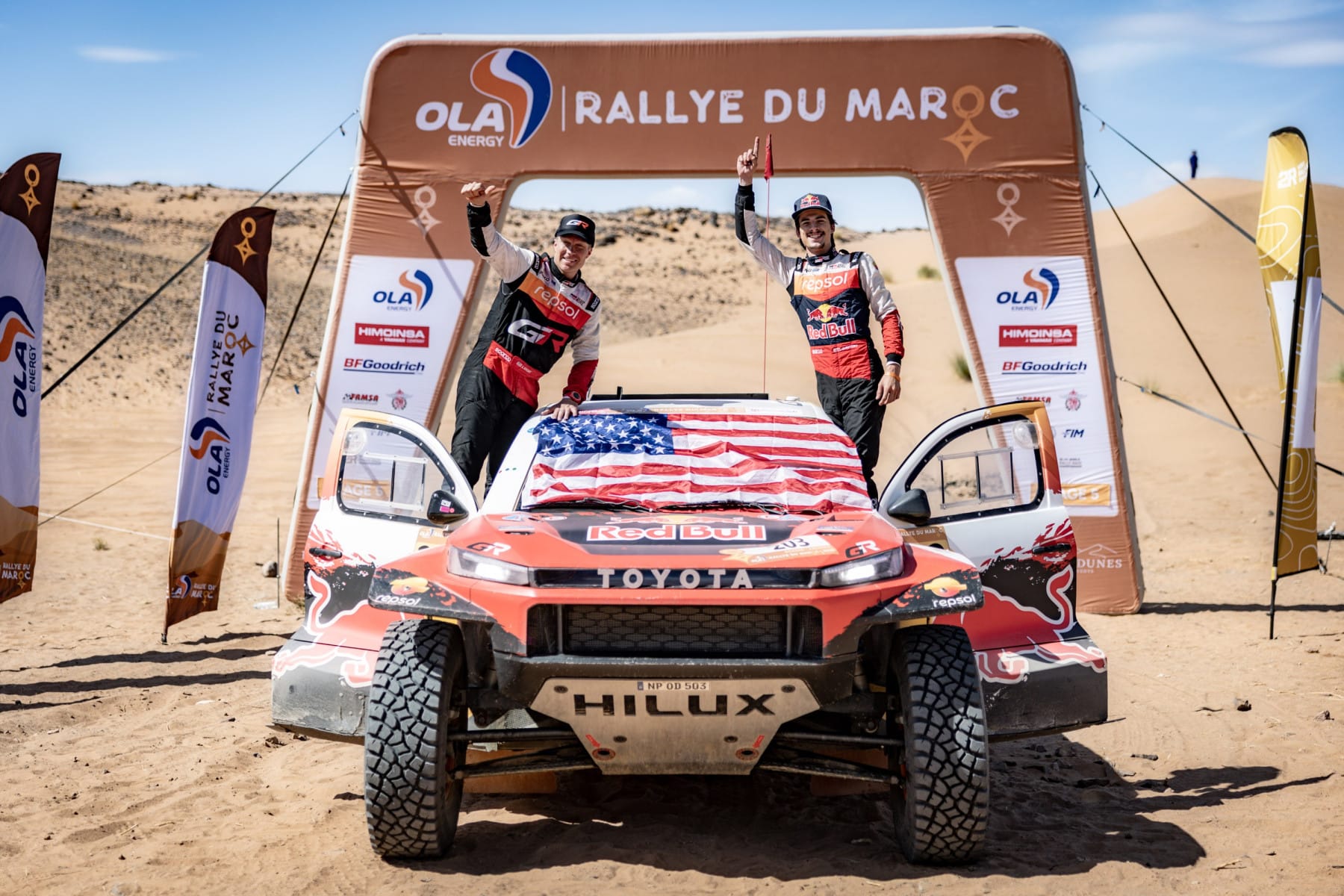 Seth Quintero y Andrew Short celebran la victoria sobre su Toyota Hilux, con la bandera de Estados Unidos, bajo el arco de meta del Rallye du Maroc